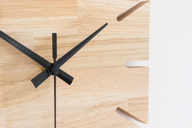 Pu&ograve; includere: Primo piano di un quadrante di orologio in legno con lancette delle ore e dei minuti nere. Il quadrante dell'orologio &egrave; in legno chiaro con una venatura naturale.