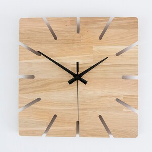 Pu&ograve; includere: Un orologio da parete quadrato in legno con lancette nere e un design unico con sezioni tagliate intorno al quadrante.