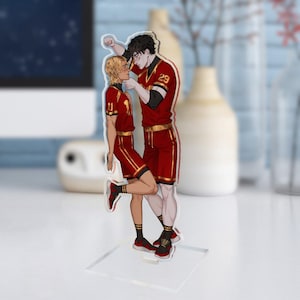 Könnte beinhalten: Eine transparente Acryl-Standfigur mit zwei Anime-Charakteren in rot-goldenen Basketball-Uniformen. Eine Figur hat blondes Haar, die andere hat schwarzes Haar. Die Figur steht auf einem transparenten Sockel.