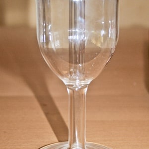 Puede incluir: Una copa de vino de vidrio transparente con un tallo alto y una base redonda. La copa tiene una pequeña pegatina azul en la base.