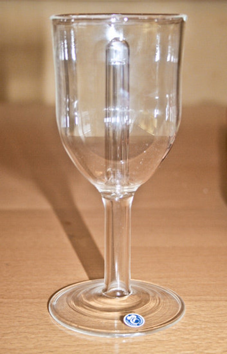 May include: A clear glass wine glass with a tall stem and a round base. The glass has a small blue sticker on the base.