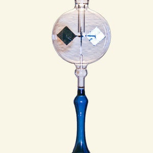 May include: A glass radiometer with a blue base and a clear glass sphere containing a rotating set of vanes. The vanes are black on one side and white on the other.
