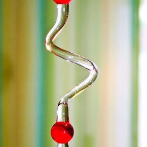 May include: A glass stem with a red glass ball on top and a red glass ball at the bottom. The stem is curved and twisted.