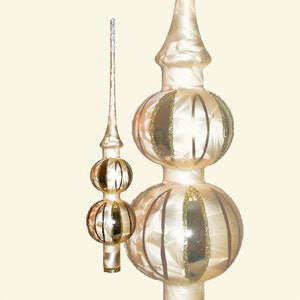 Könnte beinhalten: Ein weißer gläserner Christbaumspitzen mit goldenen Akzenten. Die Spitze hat zwei Ebenen mit runden Glühbirnen mit goldenen Streifen und einer spitzen Spitze.