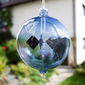 May include: A blue glass sphere with a black diamond-shaped design hanging from a silver hook. The sphere is reflecting the surrounding environment.