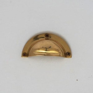 Könnte beinhalten: Ein goldfarbener Schrank-Knopf mit abgerundeter, halbkreisförmiger Form. Der Knopf hat drei sichtbare Schrauben.