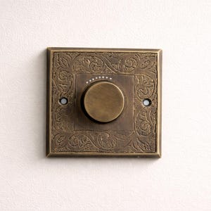 Może przedstawiać: Biały ceramiczny kubek z czarnym uchwytem i napisem "But First, Coffee" pogrubioną, czarną czcionką. Kubek jest umieszczony na rozmytym tle, podkreślając jego czysty design.