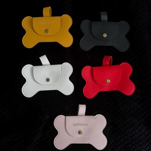 May include: Five bone-shaped pouches in yellow, black, white, red, and pink. Each pouch has a flap closure with a snap and a small handle. The pink pouch has the text "QUEEN NALA" on the flap.