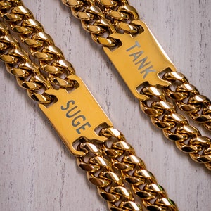 May include: Two gold chains with nameplates. The nameplate on the left chain reads "SUGE" and the nameplate on the right chain reads "TANK".