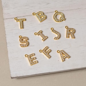 May include: A set of gold-toned letter charms with clear rhinestone embellishments. The letters are: T, B, Q, S, I, J, R, E, F, A.