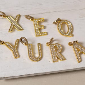 Puede incluir: Encantos de letras doradas con adornos de cristal transparente. Las letras deletrean el nombre "YURA".