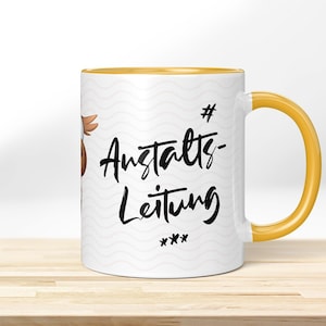 Puede incluir: Taza de cerámica blanca con borde y asa amarillos. La taza tiene un patrón ondulado y el texto "# Anstalts- Leitung ***" en negro.