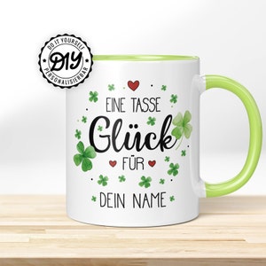 Könnte beinhalten: Weiße Keramiktasse mit grünem Rand und Henkel. Die Tasse hat ein Design aus grünen vierblättrigen Kleeblättern und dem Text "Eine Tasse Glück für Dein Name".