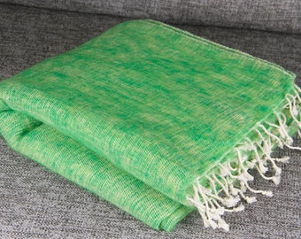 Pode incluir: Um cobertor verde e branco tecido dobrado com uma borda com franjas. O cobertor é de cor verde brilhante com detalhes em branco e está cuidadosamente dobrado. A franja é branca. O cobertor está sobre uma superfície cinza.