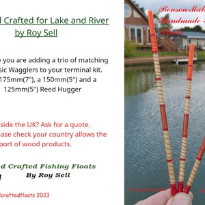 May include: Three orange and red fishing floats, made of wood, with a brown and white striped pattern. The floats are held in a hand against a background of a lake and houses.