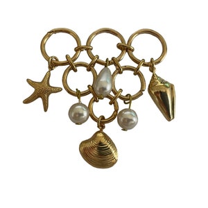 May include: Gold charm bracelet with a variety of sea-themed charms, including a starfish, seashells, and pearls.