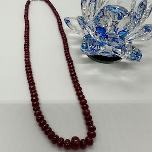 Op de afbeelding: Een lange ketting gemaakt van donkerrode kralen. De ketting is gemaakt van ronde kralen en heeft een zilveren sluiting.