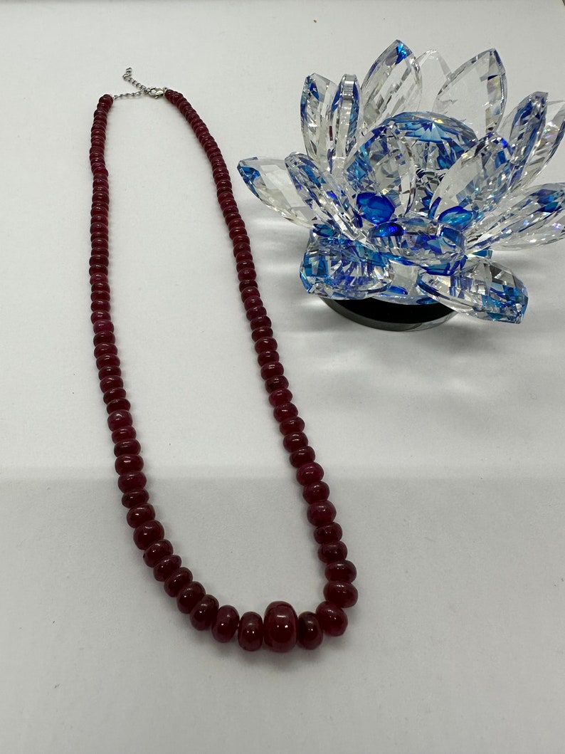 May include: A long necklace made of dark red beads. The necklace is made of round beads and has a silver clasp.