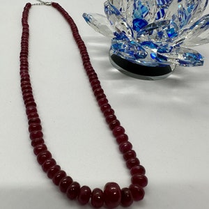 May include: A long necklace made of dark red beads. The necklace has a silver clasp and a larger, round bead in the center.