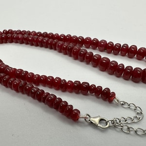 May include: A red gemstone beaded necklace with a silver clasp and chain.