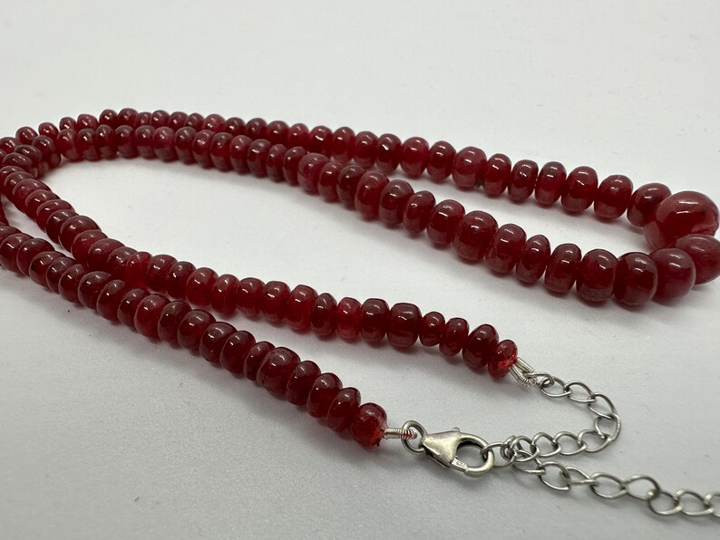 May include: A red gemstone beaded necklace with a silver clasp and chain.
