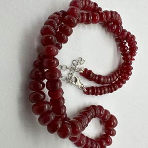 May include: A red gemstone bead necklace with a silver clasp. The necklace is made of round beads and is approximately 18 inches long.