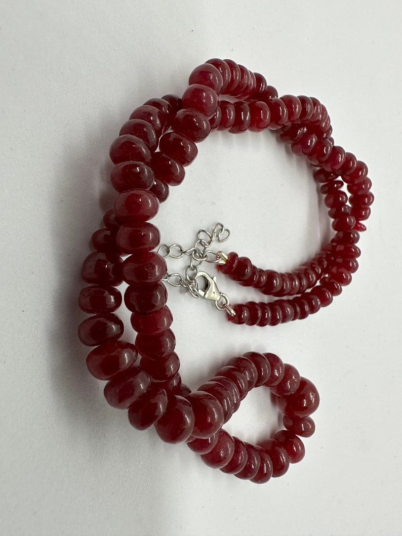 May include: A red gemstone bead necklace with a silver clasp. The necklace is made of round beads and is approximately 18 inches long.