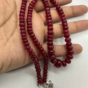 May include: A red gemstone necklace with a silver clasp. The necklace is made of round beads and is approximately 18 inches long.