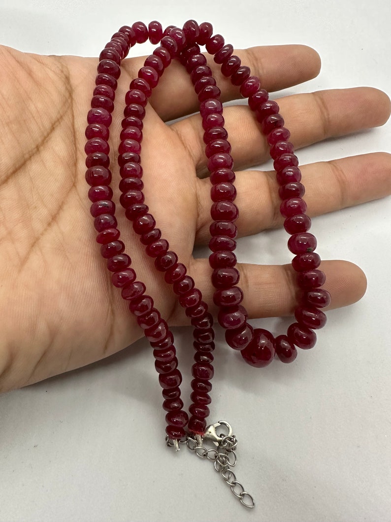 May include: A red gemstone necklace with a silver clasp. The necklace is made of round beads and is approximately 18 inches long.