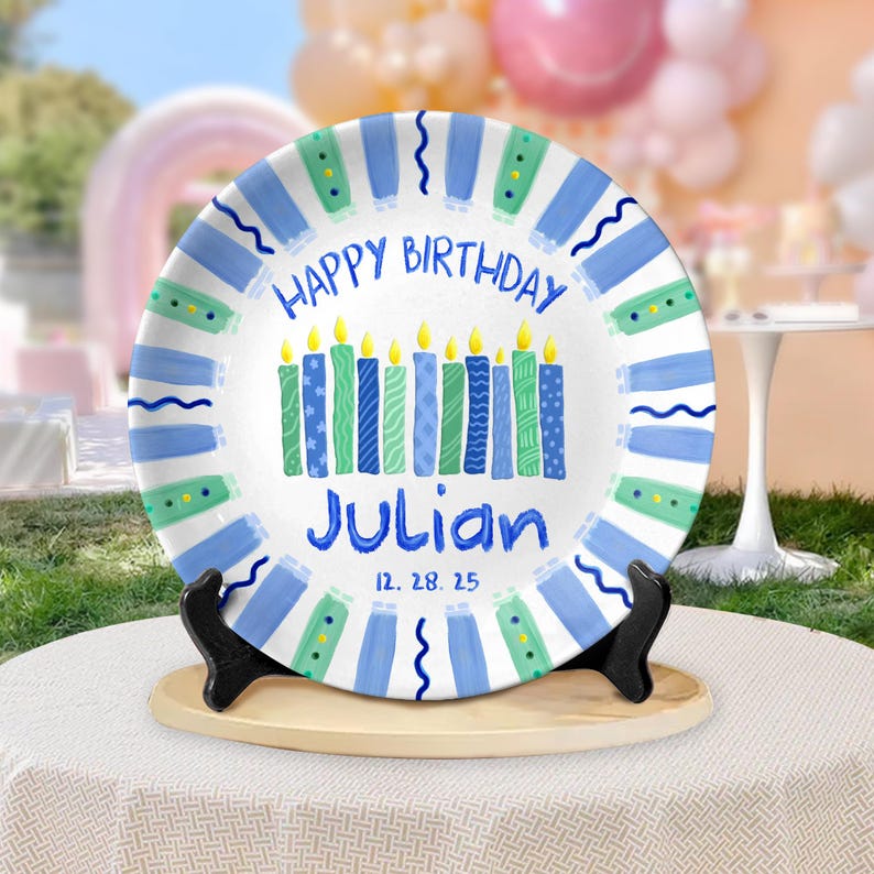 May include: A white plate with a blue and green striped border and the words "HAPPY BIRTHDAY" and "Julian" in blue. The plate features candles with yellow flames and the date 12.28.25.