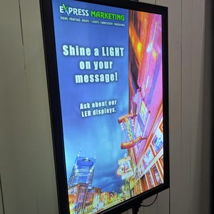 May include: A black framed LED sign with a cityscape background. The sign reads "EXPRESS MARKETING" and "Shine a LIGHT on your message! Ask about our LED displays."