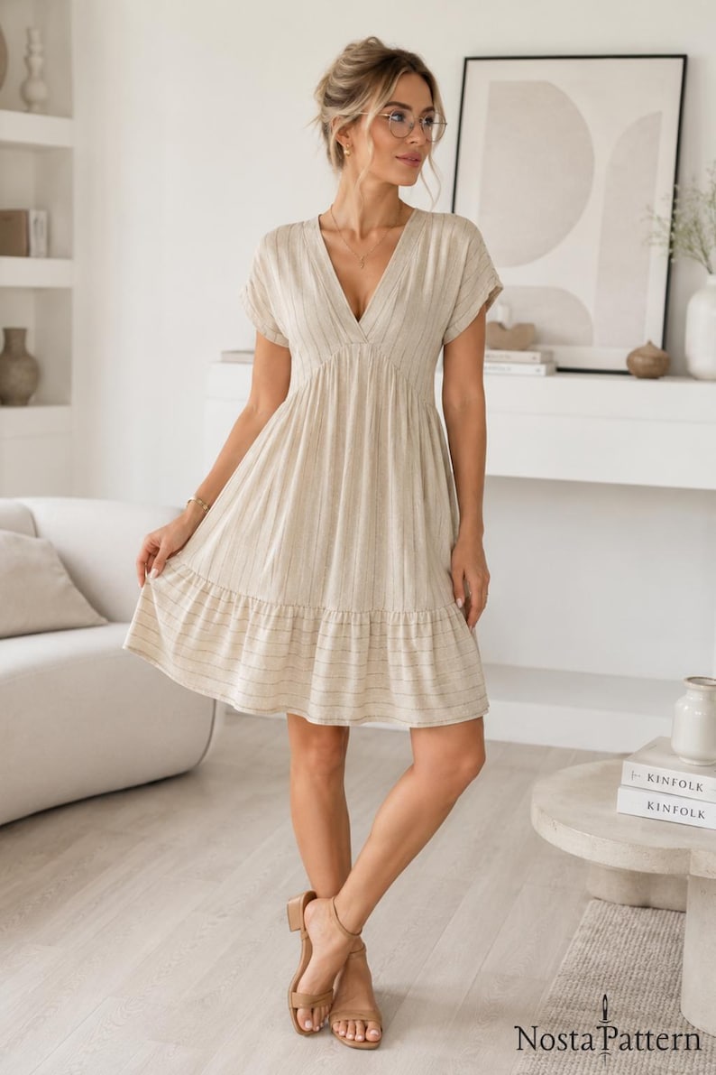 May include: A beige knee-length dress with a V-neckline, short sleeves, and a gathered skirt featuring a subtle vertical stripe pattern. The dress has a tiered hemline and is made of a textured fabric. The text Nosta Pattern is visible.