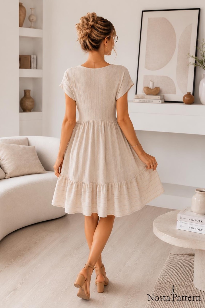 May include: A beige knee-length dress with short sleeves, a fitted bodice, and a flared skirt featuring a horizontal striped pattern at the hem. The garment has a V-neckline and a textured fabric finish, shown from the back view.