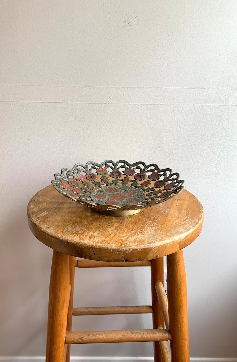 Może przedstawiać: Dekoracyjna miedziana miska z filigranowym wzorem i kolorowymi akcentami. Miska stoi na drewnianym stołku.