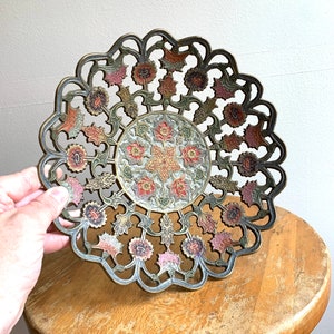 Może przedstawiać: Dekoracyjna miedziana miska z misternym wzorem kwiatowym. Miska jest pomalowana w odcieniach r&oacute;żowego, zielonego i złotego.