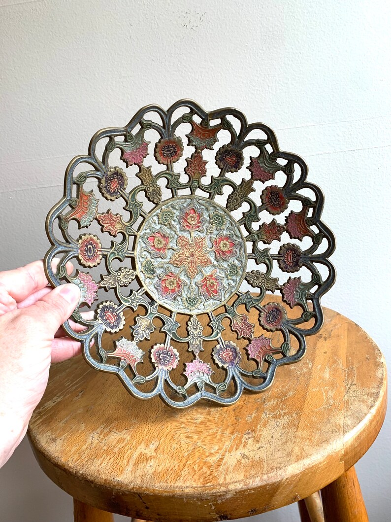 Może przedstawiać: Dekoracyjna miedziana miska z misternym wzorem kwiatowym. Miska jest pomalowana w odcieniach r&oacute;żowego, zielonego i złotego.