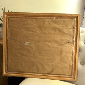 May include: A wooden picture frame with a brown paper backing and a wire hanger. The frame has a simple, rustic design.