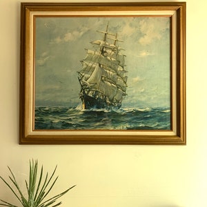 May include: A framed vintage print of a ship with white sails sailing on a blue ocean under a cloudy sky.