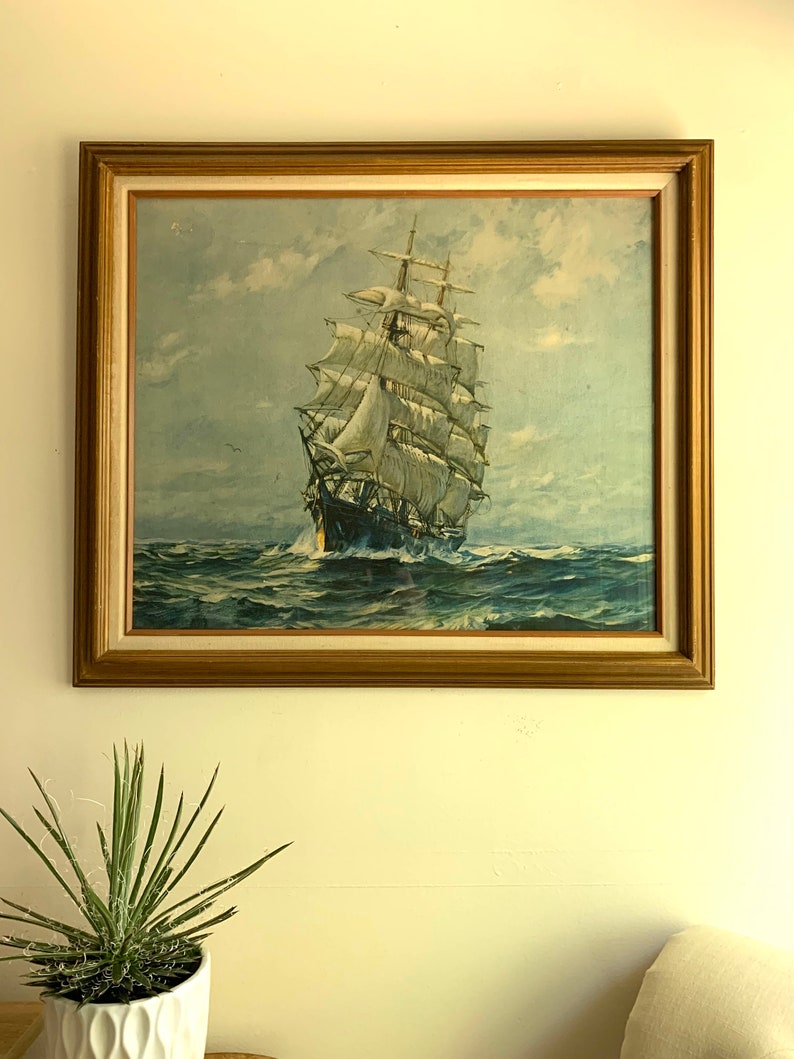 May include: A framed vintage print of a ship with white sails sailing on a blue ocean under a cloudy sky.