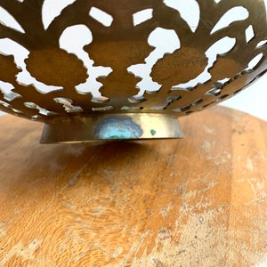 Może przedstawiać: Miska mosiężna z ozdobnym wzorem wyciętym. Miska ma falisty brzeg i okrągłą podstawę.