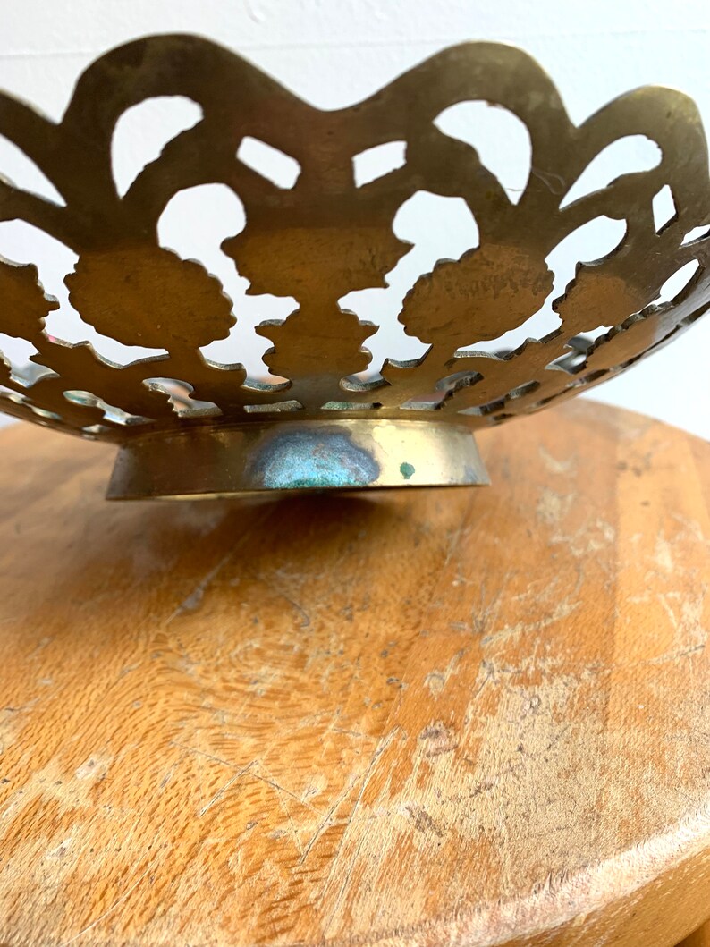 Może przedstawiać: Miska mosiężna z ozdobnym wzorem wyciętym. Miska ma falisty brzeg i okrągłą podstawę.