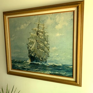 May include: A framed painting of a large sailing ship with white sails on a blue ocean under a cloudy sky.