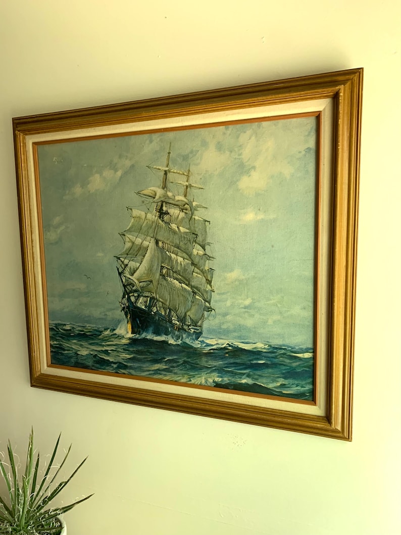 May include: A framed painting of a large sailing ship with white sails on a blue ocean under a cloudy sky.