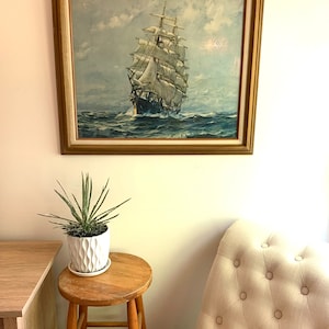 May include: A framed vintage print of a sailing ship with white sails against a blue sky and ocean. The ship is in the center of the image and is surrounded by water. The frame is gold and has a white mat.
