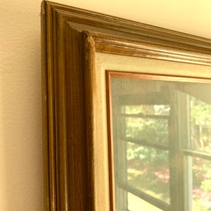 May include: A framed artwork with a brown wooden frame and a canvas backing. The artwork depicts a blurry view of a window with a green landscape outside.