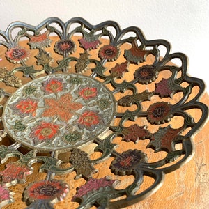 Może przedstawiać: Dekoracyjna miedziana tacka do serwowania z misternym wzorem kwiatowym. Tacka wykonana jest z mosiądzu i ma złote, zielone, czerwone i białe wykończenie. Tacka idealnie nadaje się do serwowania przekąsek, przystawek lub deser&oacute;w.