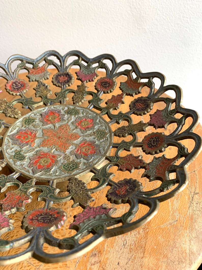 Może przedstawiać: Dekoracyjna miedziana tacka do serwowania z misternym wzorem kwiatowym. Tacka wykonana jest z mosiądzu i ma złote, zielone, czerwone i białe wykończenie. Tacka idealnie nadaje się do serwowania przekąsek, przystawek lub deser&oacute;w.