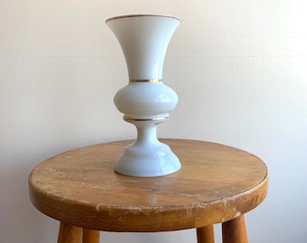 May include: White ceramic vase with a gold rim and a round base. The vase is sitting on a wooden stool.