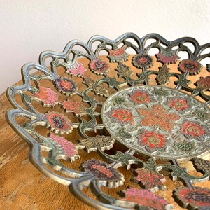 Może przedstawiać: Dekoracyjna miedziana miska z misternym wzorem kwiatowym. Miska jest wykonana z metalu i ma falisty brzeg. Wz&oacute;r przedstawia kwiaty w odcieniach r&oacute;żowego, czerwonego i zielonego.