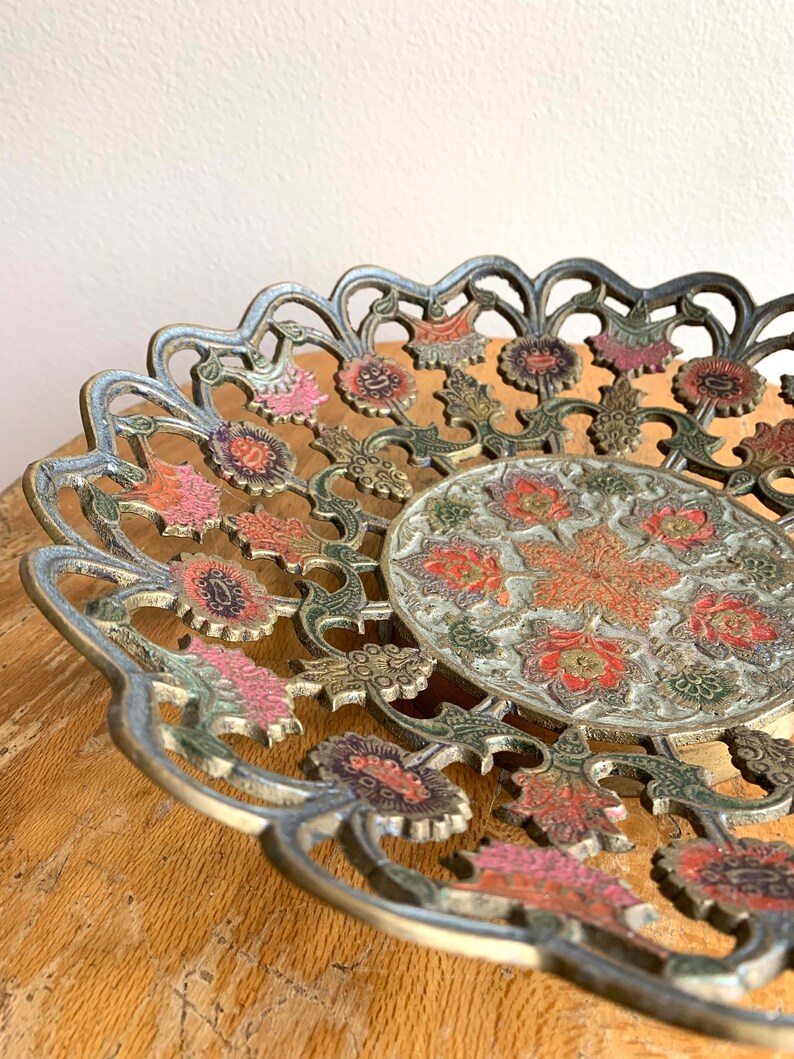 Może przedstawiać: Dekoracyjna miedziana miska z misternym wzorem kwiatowym. Miska jest wykonana z metalu i ma falisty brzeg. Wz&oacute;r przedstawia kwiaty w odcieniach r&oacute;żowego, czerwonego i zielonego.